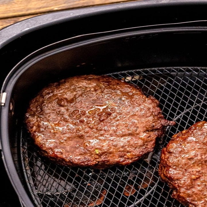 Two burger patties in the basket of an air fryer.