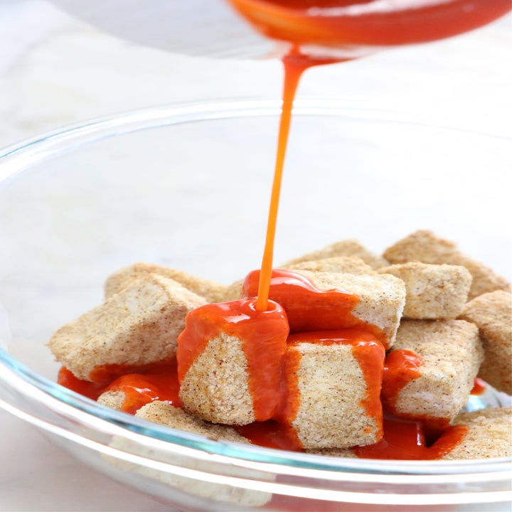 Pouring buffalo sauce on crispy tofu bites.